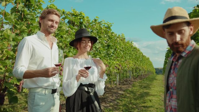 Winemaker in strawhat guiding exciting wine tour for wealthy couple of guests. Romantic tourists visiting winery on holiday.