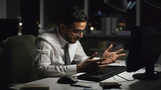 Medium shot of exhausted Arab businessman working on computer in office at night, then hitting keyboard in frustration