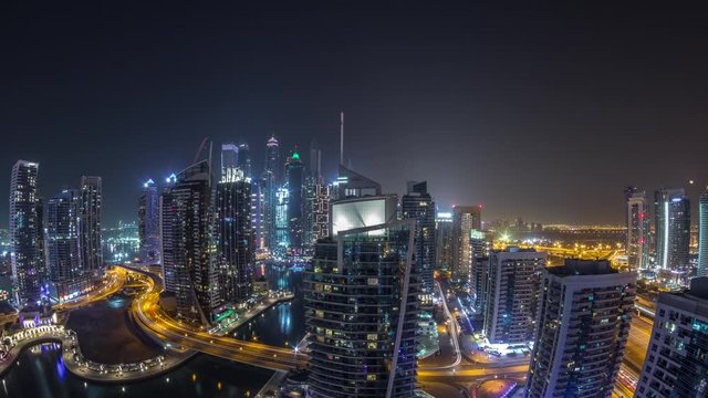 Aerial panoramic view of Dubai Marina residential and office skyscrapers with waterfront during all night timelapse with lights switching off. Floating boats and yachts
