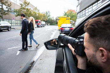 Male Spy Taking Photograph Of A Couple Walking On Street