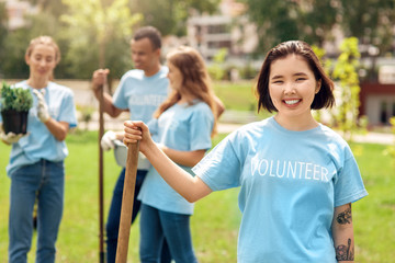 Volunteering. Young people volunteers outdoors planting trees asian girl close-up standing with shovel smiling cheerful blurred background