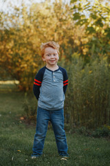 Portrait of Caucasian red-haired cute handsome preschool boy. Adorable child standing outside on autumn fall day. Happy smiling kid outdoor. Authentic lifestyle childhood.