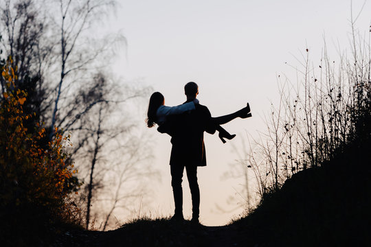 Silhouette of a man who holds a girl in his arms. Back view.
