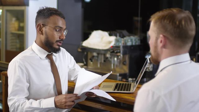 Middle eastern and caucasian businessmen reading and discussing contract beside bar counter in cafe