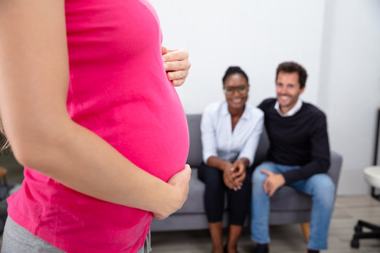 Pregnant Woman In Front Of Couple Sitting On Sofa