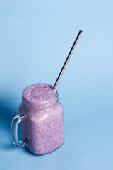 Blueberry smoothie drink in mason jar glass with reusable stainless steel straw on blue background