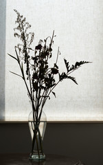 Dead flowers and branches on a transparent glass vase against a white cloth background