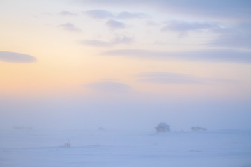 Winter landscape with a small abandoned house in a snow-covered tundra. Cold weather, blowing snow. Dawn. Chukotka, Siberia, Far North of Russia, Arctic.