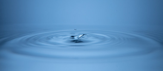 Water droplet falling onto calm still water, splash forming concentric circles