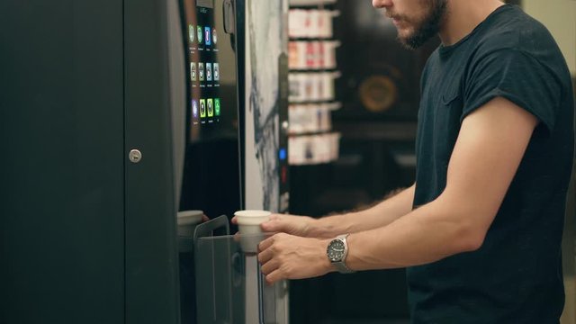 Young Man Stirring Coffee from Vending Machine