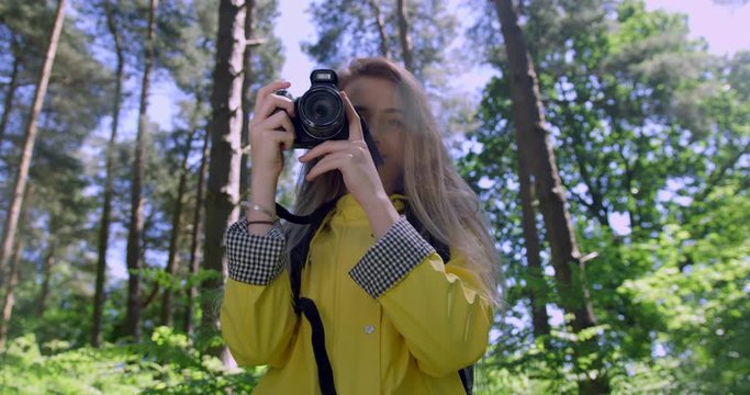  Young Woman with Camera in the Forest. Girl taking Photographs in a Woodland Glade wearing a Yellow Rain Coat. Happy, blonde Student Girl within Trees at a Green Natural Park with Sun Light Flare.