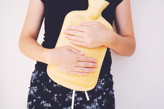 Extreme close-up mid section of a woman holding yellow hot water bag on abdomen