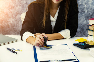 Female notary stamping document agreement at table, close up.