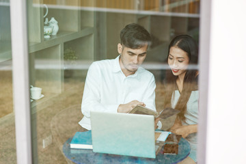 Portrait of two asian co-workers talking in office. Young business colleagues looking at the screen of tablet pc while discussing work. Horizontal shot. View from the window