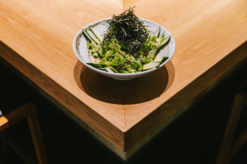 Japanese cucumber salad with lettuce, radish and dry seaweed served in ceramic bowl on wooden counter.