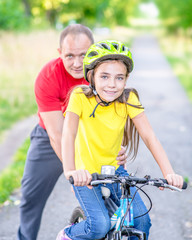 Happy family. Smiling fatherteaches his daughter to ride a bicycle in the summer park