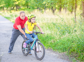 Father helps daughter learn to ride a bike in summer park