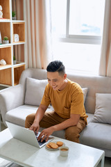 Young man is browsing at his laptop and calling with customer on the sofa at home, Business success