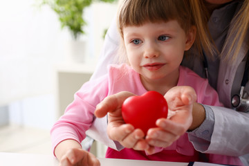 Female doctor and happy little child hold in arms red toy heart closeup. Cardio therapeutist student education CPR 911 life save physician make cardiac physical pulse rate measure arrhythmia lifestyle