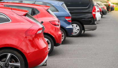 Closeup of rear, back side of red car with  other cars parking in outdoor parking area.
