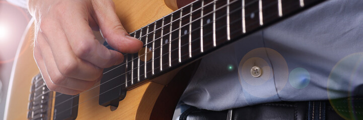 Obraz premium Male arms holding and playing classic shape wooden electric guitar closeup. Six stringed learning musical school education art leisure electrical vintage stage shop having fun enjoying hobby concept