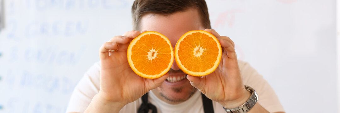 Man holds halves of cut orange as eye glasses portrait background concept
