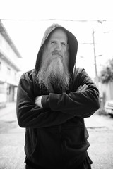 Mature bald man with long gray beard with arms crossed outdoors