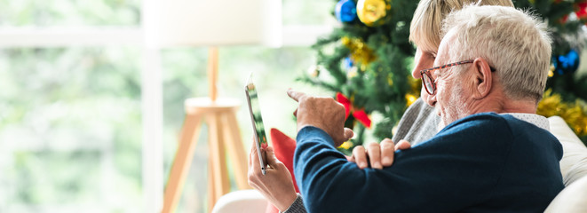 Christmas online shopping. Senior caucasian man and woman sitting on couch using tablet in living room. Browsing the internet. Banner frame.