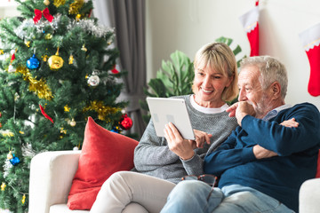 Christmas online shopping. Senior caucasian man and woman sitting on couch using tablet in living room. Exciting look.