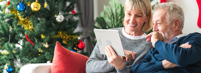 Christmas online shopping. Senior caucasian man and woman sitting on couch using tablet in living room. Very excited. Banner frame.