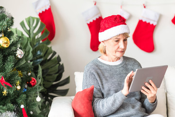 Christmas online shopping. Senior caucasian woman sitting on couch using tablet in living room. Focusing on what to get.