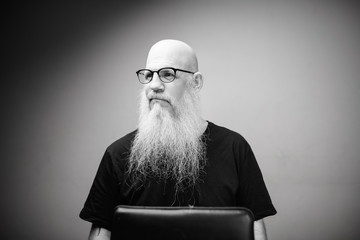 Thoughtful mature bald man with long gray beard wearing eyeglasses in black and white