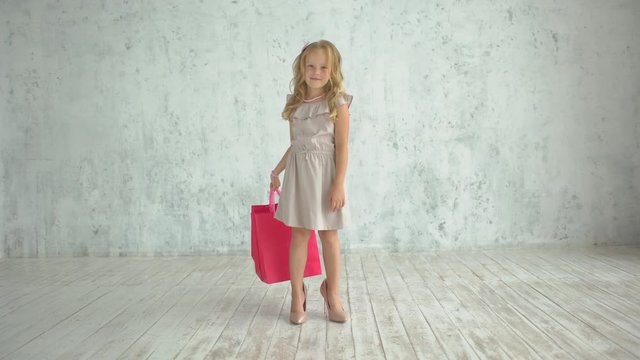 family shopping, bags, shopping girl. funny child little girl fashionista in big mother's shoes in dress with shopping bag. Girl in big shoes holding packages in hand. baby fashion concept, 4 K