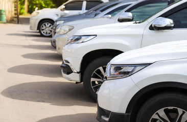 Closeup of front side of white car and other cars parking in outdoor parking area.