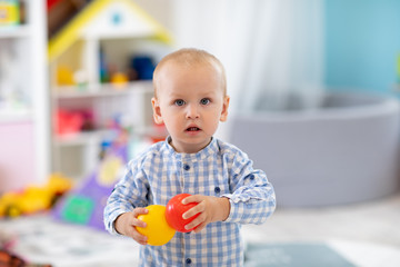 Adorable one year old baby in play room. Child boy playing with colorful toys at home. Early...