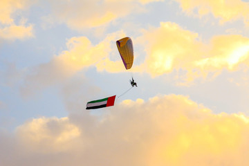 a man flying at the sunset holding uae flag, uae flag waving at the sunset, Flying paraglider with uae flag , uae flag day. united arab emirates 
