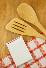 Notepad, tablecloth, spatula and spoon on wooden table, cooking and recipe concept