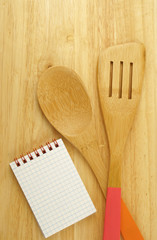 Spatula, notebook and spoon on wooden table background 