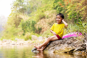 Adorable Asian girl sitting on riverside rock with her pool ring aside