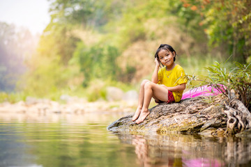 Adorable Asian girl sitting on riverside rock with her pool ring aside