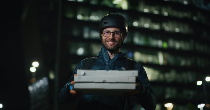 Portrait of an young pizza delivery courier is smiling satisfied with his work in the camera in the evening in a city center.