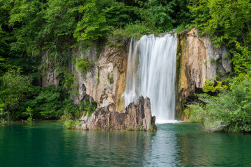 Fototapeta na wymiar Crystal clear, pure water rushing down mossy rocks into a beautiful azure colored lake at the Plitvice Lakes National Park in Croatia