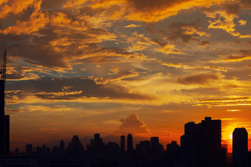 Sunset sky with silhouetted buildings in city. Warm sky in cloudy day.