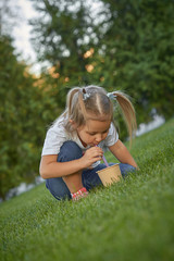 Fototapeta premium Beautiful little girl outdoors in a park. Lifestyle happy portrait of a little girl outdoors in a meadow. Child drinks cocoa