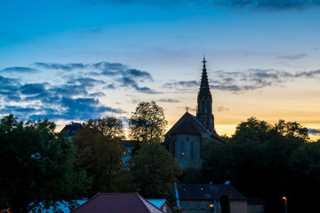 Fototapeta premium Germany, Beautiful sunset sky decorating medieval ancient church and skyline of stuttgart district berg, called berger church surrounded by trees, seen from above the roofs HDR