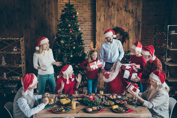 Photo of large family with small little kids senior pensioner sit table on x-mas meal celebration in santa claus cap hat get receive wish gift boxes house having x-mas tree atmosphere spirit