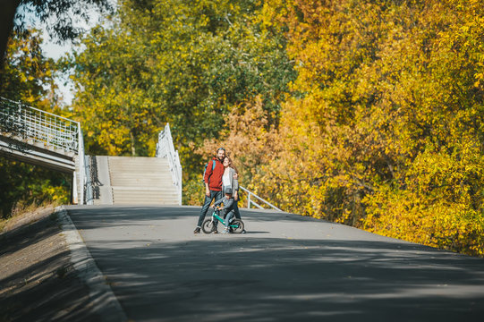 Mother, father and little son on bike poses in autumn park at the distance in the sunny day