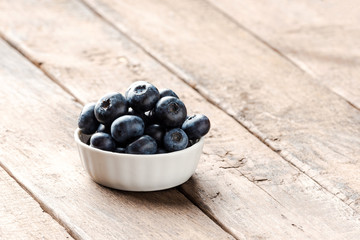 Fresh blueberries in small bowl on wooden table. Close up