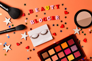 Beauty blogger text on an orange background. Professional trendy makeup products with cosmetic beauty products,  eye shadows, eye lashes, brushes and tools.