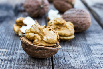 Peeled walnuts and walnut kernels lie on a rustic old wooden table.